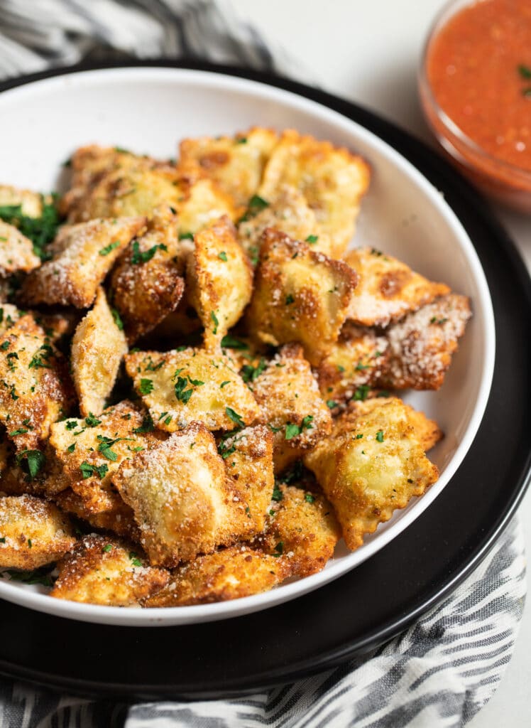 Fried ravioli in a bowl served with marinara sauce.