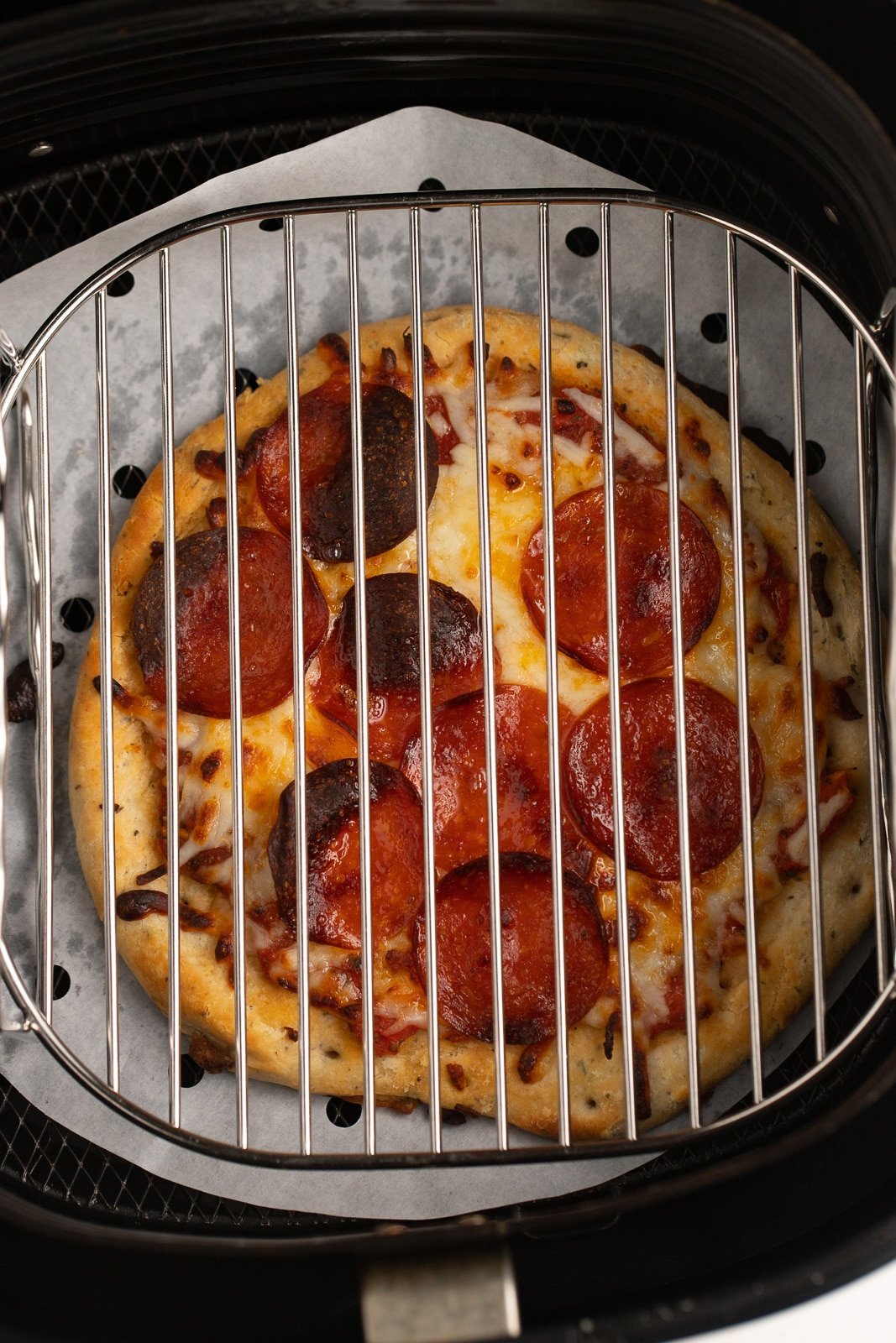 The cooked pizza in the air fryer basket with a rack over the top.
