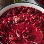 Beet soup served in a white bowl with a spoon.