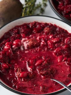 Beet soup served in a white bowl with a spoon.