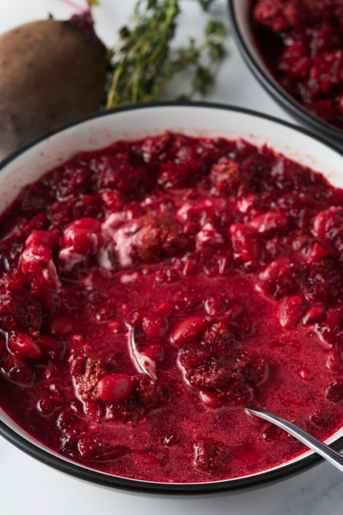 Beet soup served in a white bowl with a spoon.