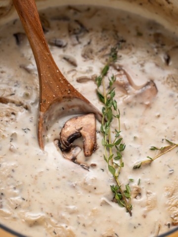 A wooden spoon in a pot of cream of mushroom soup.