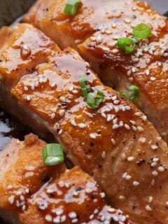 teriyaki salmon in a pan with green onion and sesame seed on top