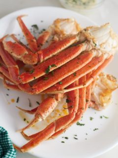 Air fryer crab legs on a white plate and garnished with herbs.