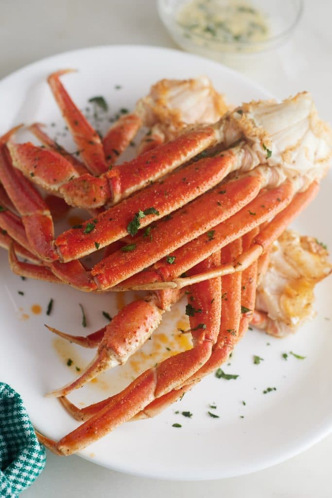 Air fryer crab legs on a white plate and garnished with herbs.