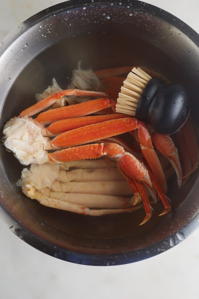 crab legs in large bowl with water and scrubber