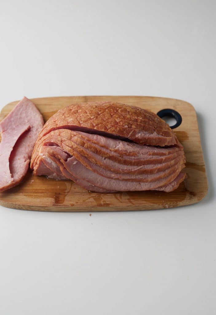 The ham sliced on a wooden chopping board.
