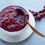 Cranberry sauce served in a white bowl with a gold spoon.