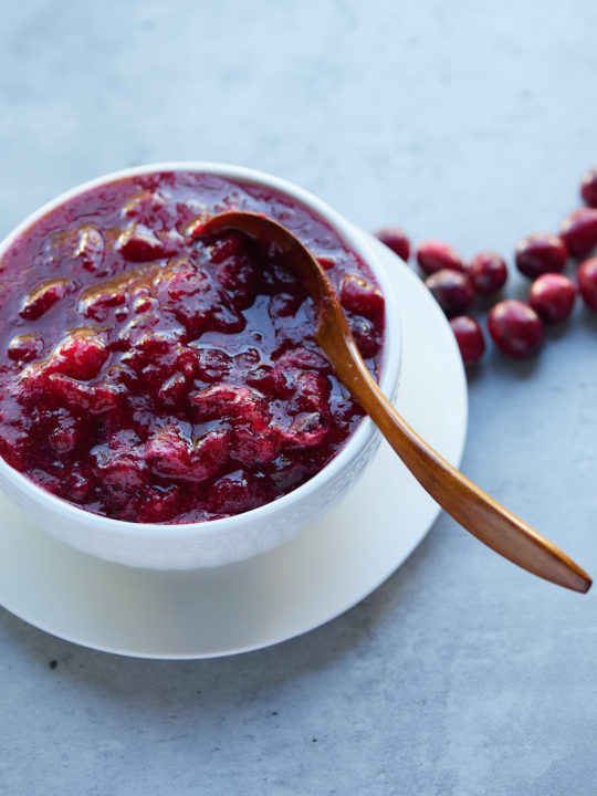 Cranberry sauce served in a white bowl with a gold spoon.