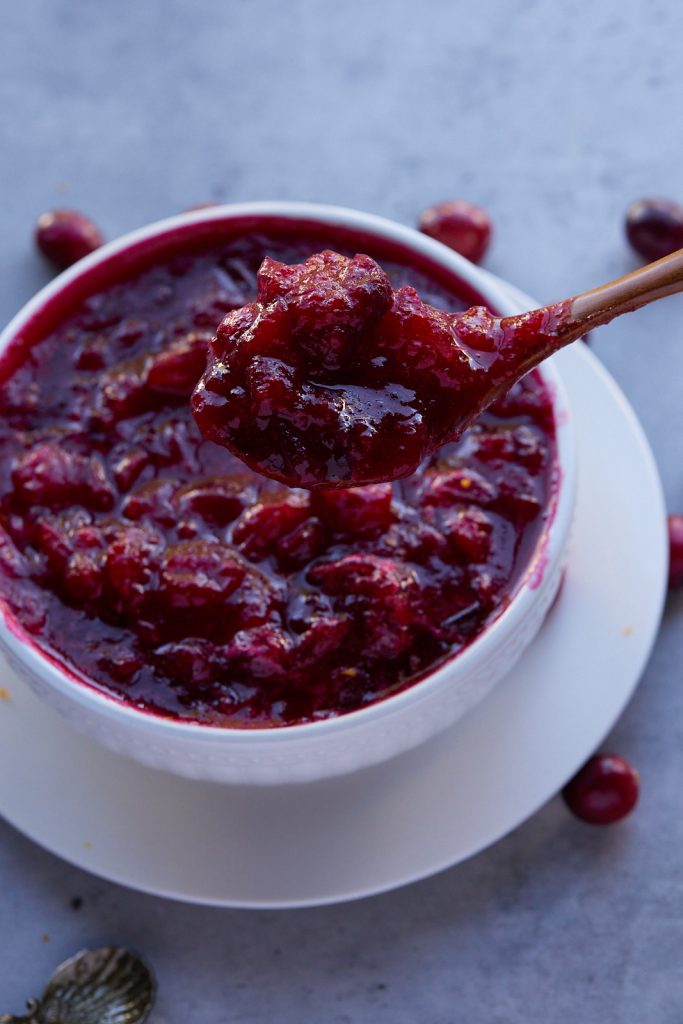A gold spoon in a white bowl of cranberry sauce.