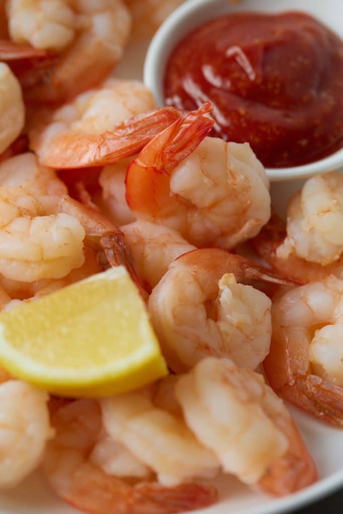 Close up of cooked shrimp served with cocktail sauce and a lemon wedge.