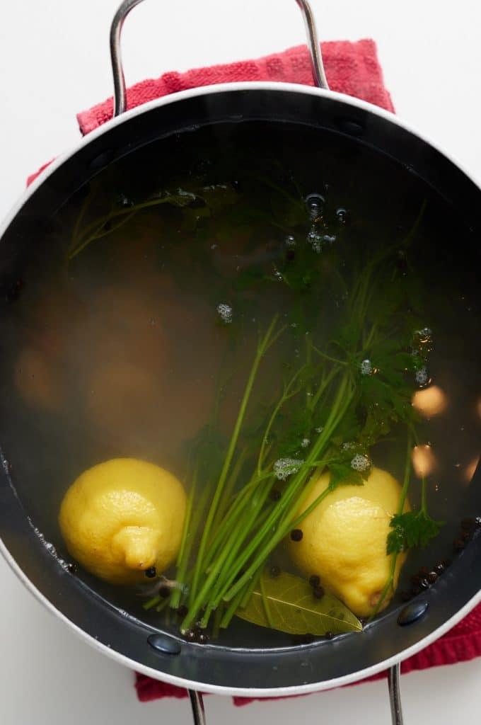 Shrimp cooking in a pot of water with lemon and herbs.