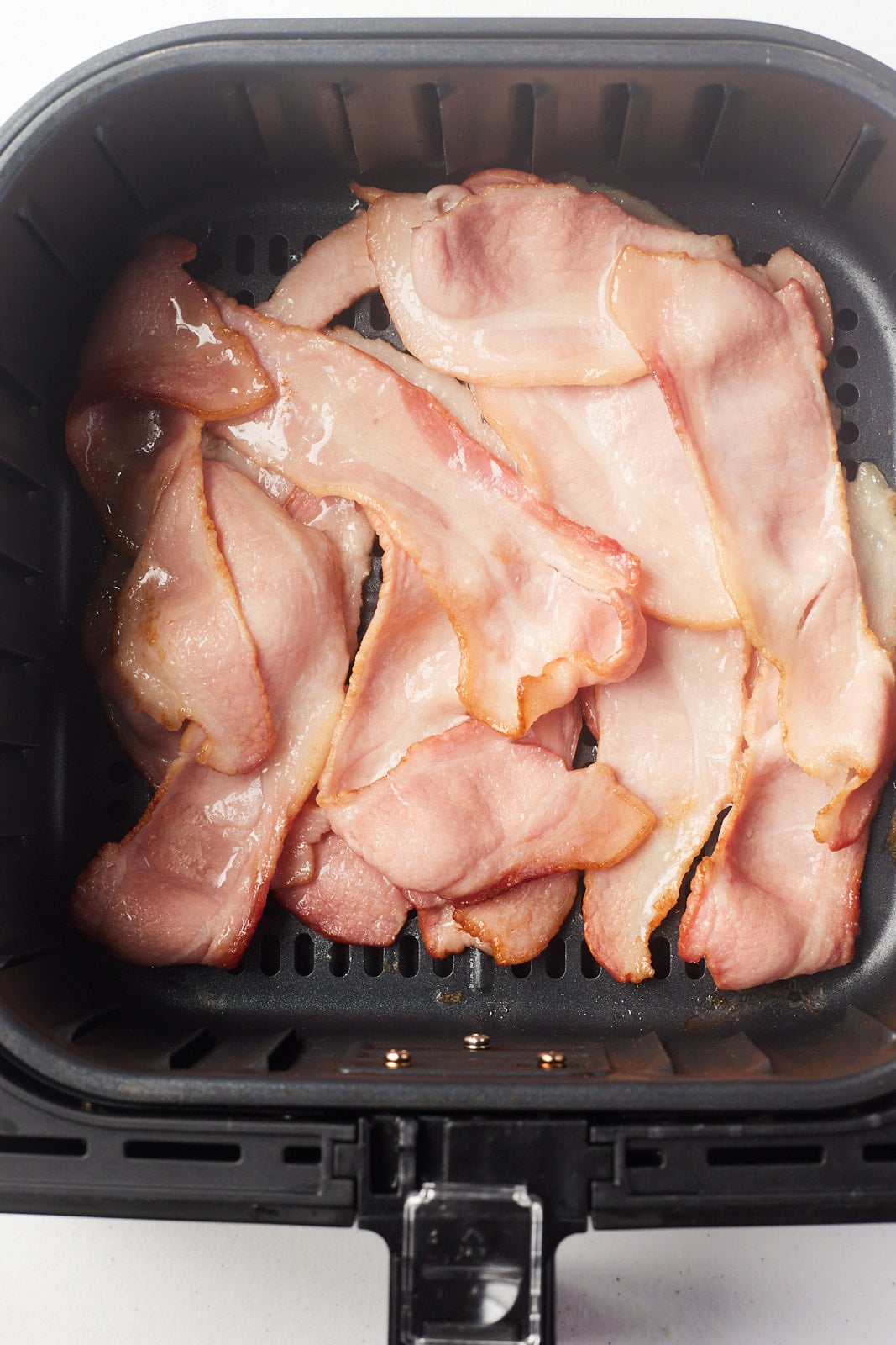 Bacon starting to cook the air fryer basket.