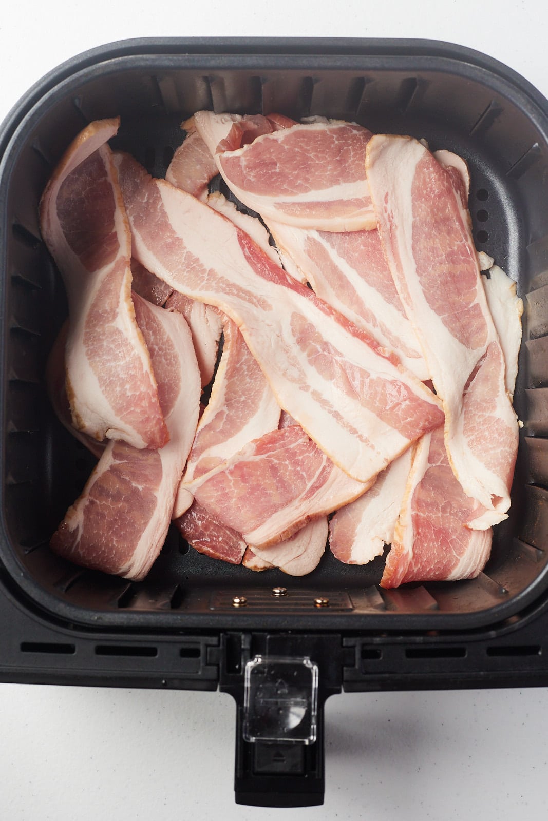 Raw bacon strips in an air fryer basket.
