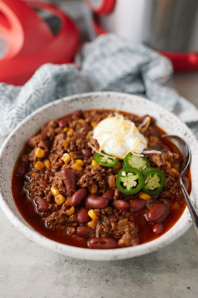 A bowl of pressure cooker chili with a spoon in it and served with toppings.