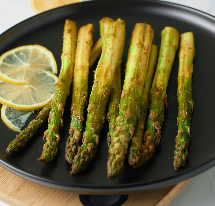 Asparagus served on a plate with slices of lemon.