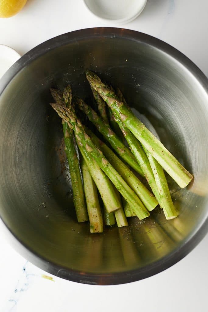 Asparagus stems being seasoned in a bowl.