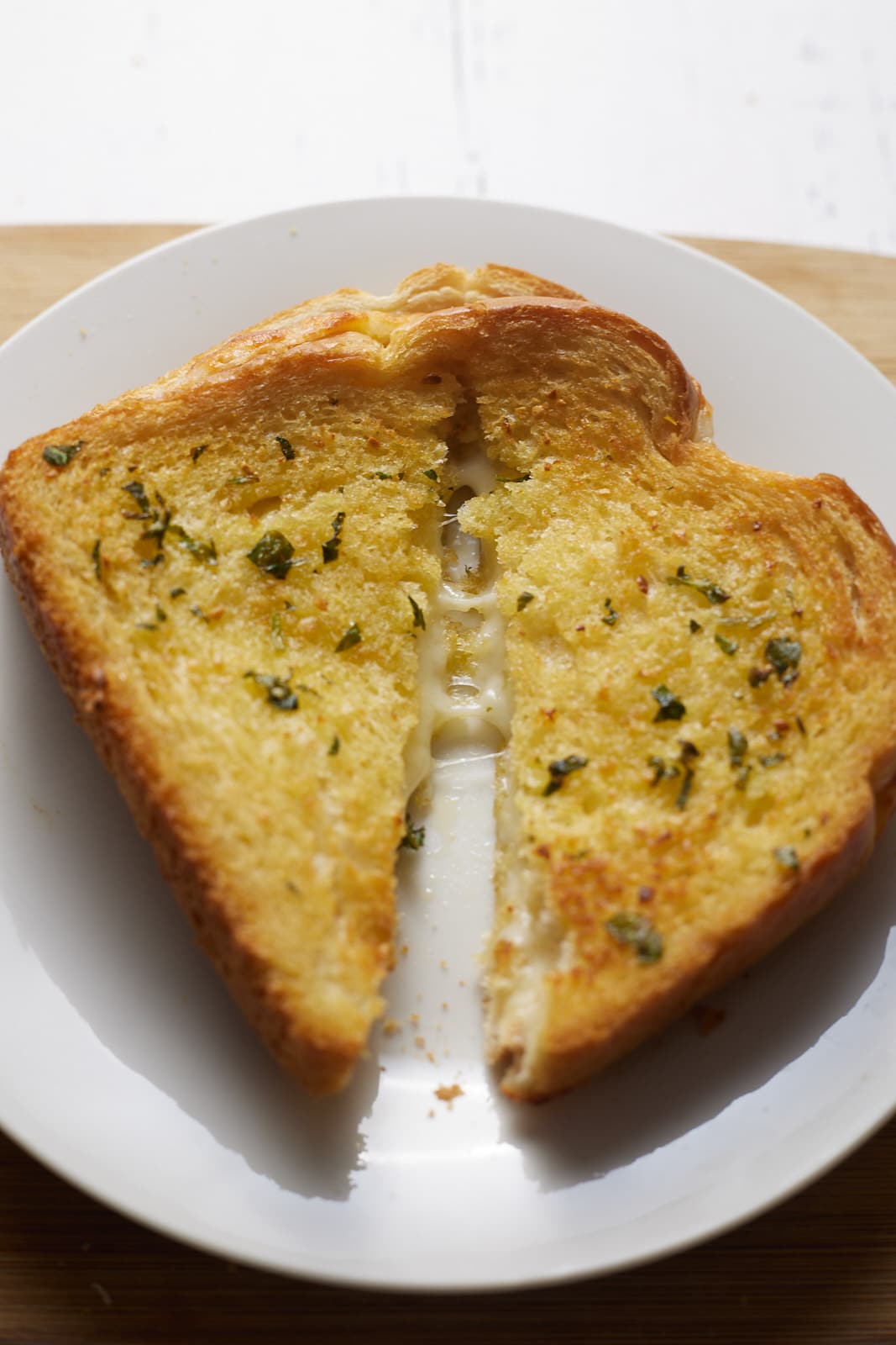 A grilled cheese sandwich on a white plate cut into two triangles.