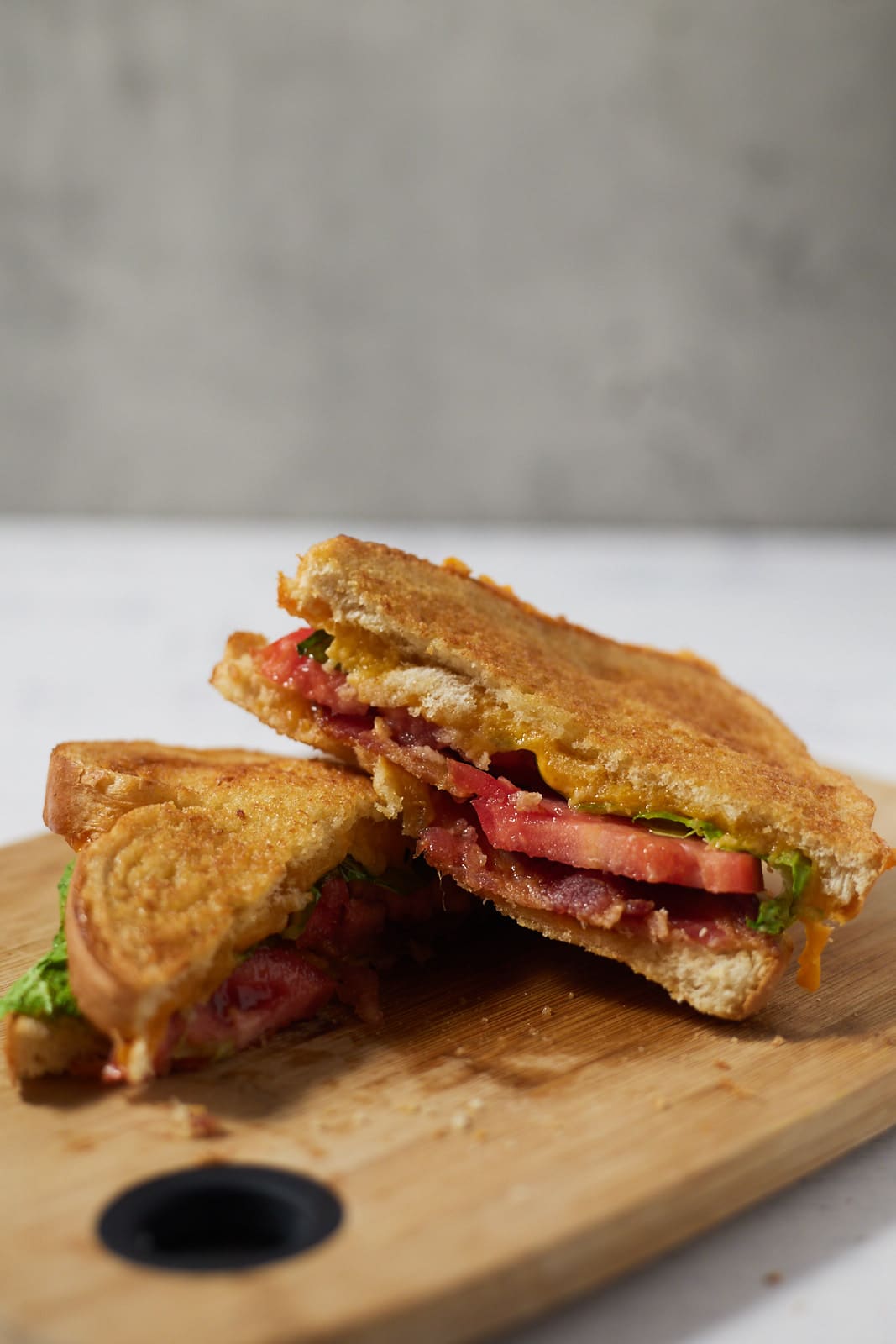 A BLT grilled cheese cut in half on a wooden chopping board.