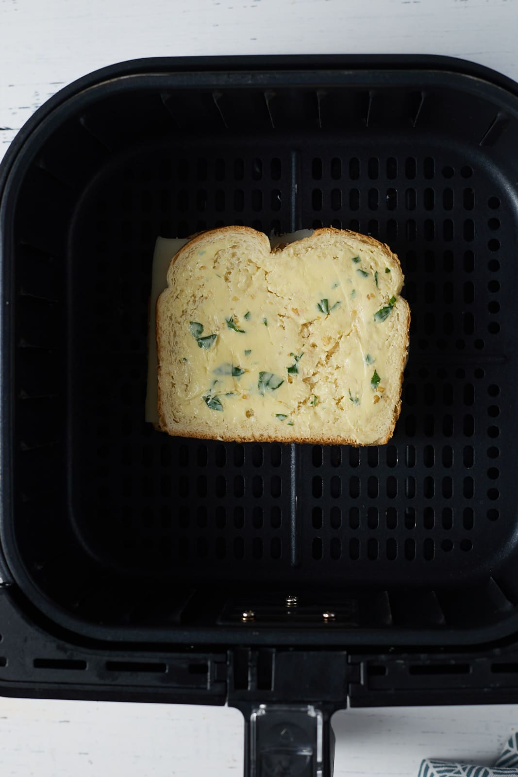 A grilled cheese in the air fryer basket before being cooked.