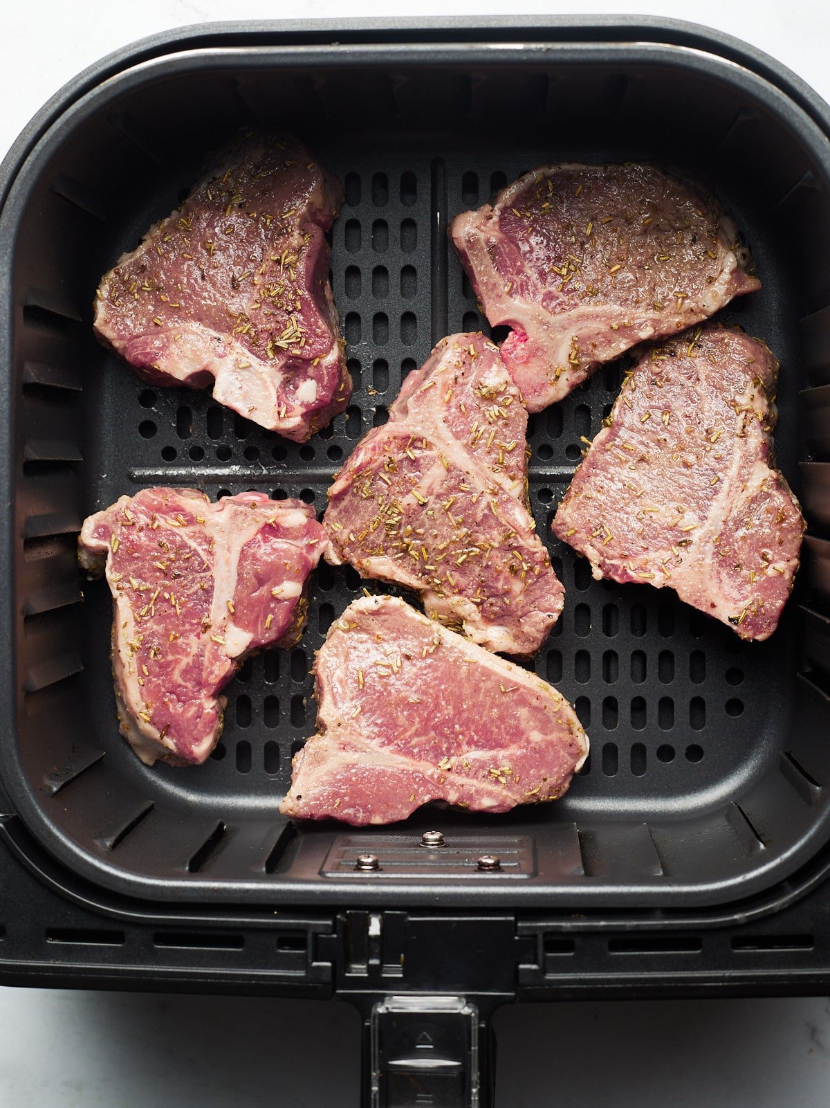 Raw lamb chops placed in the air fryer basket.