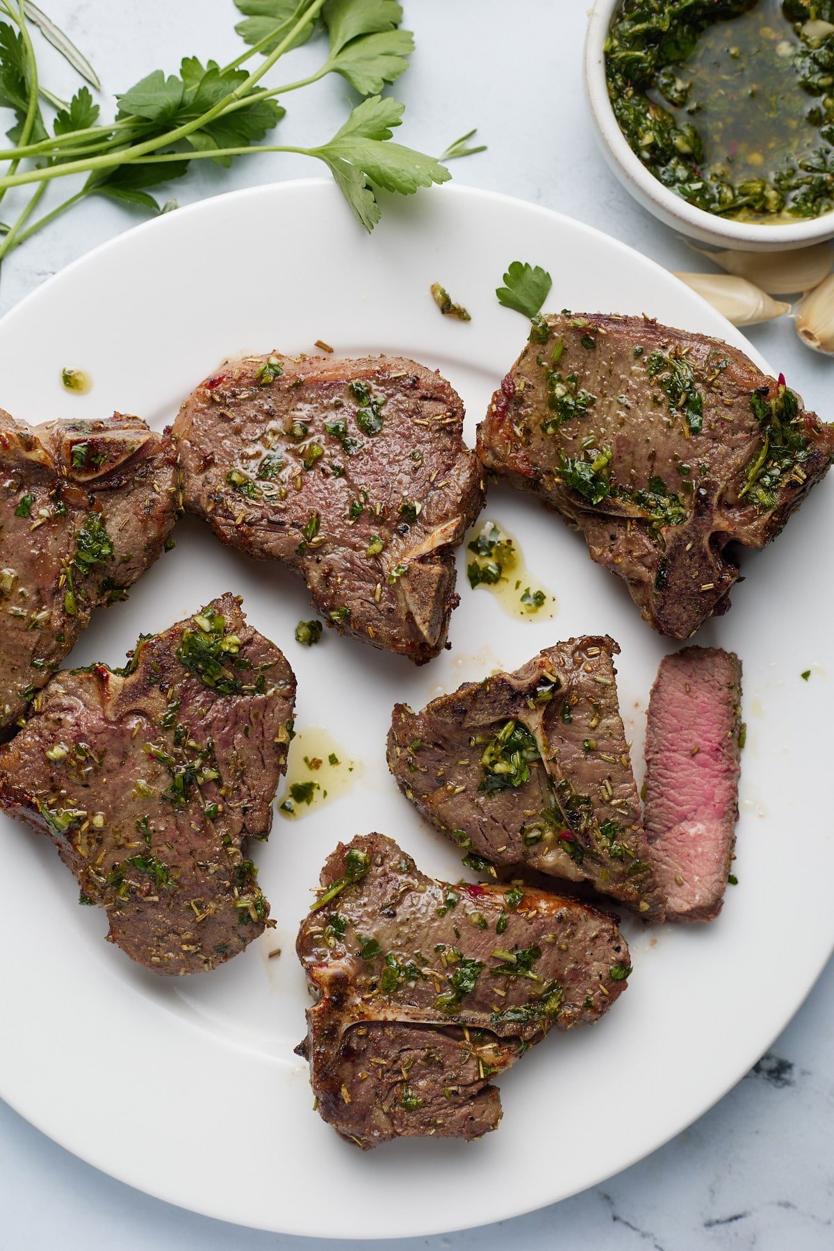 Six cooked lamb chops on a white plate.