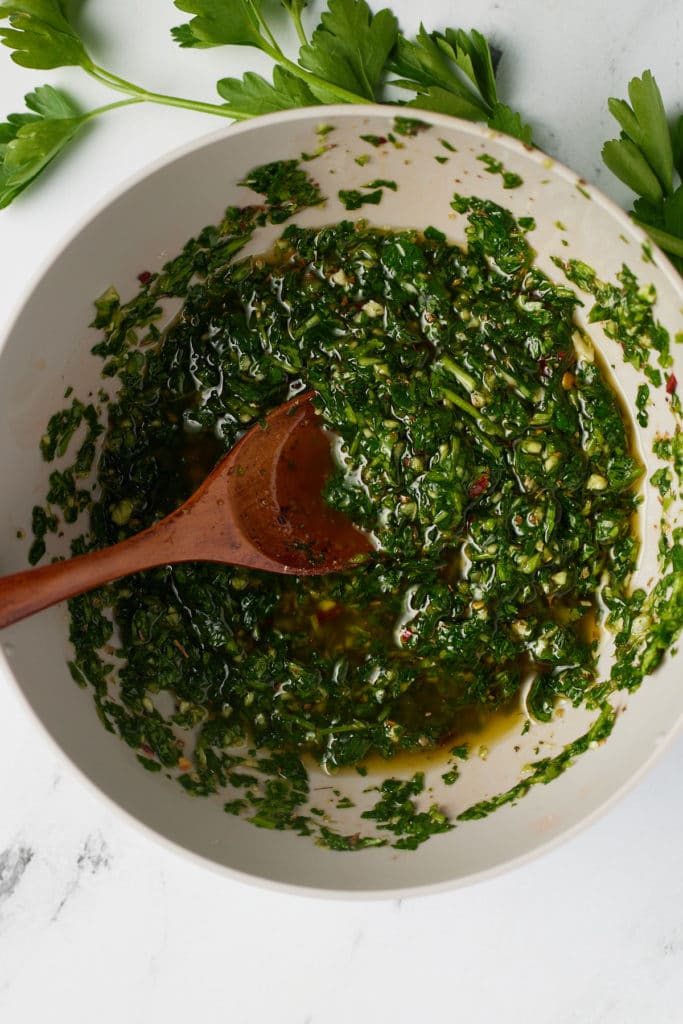 Chimichurri served in a white bowl with a wooden spoon.