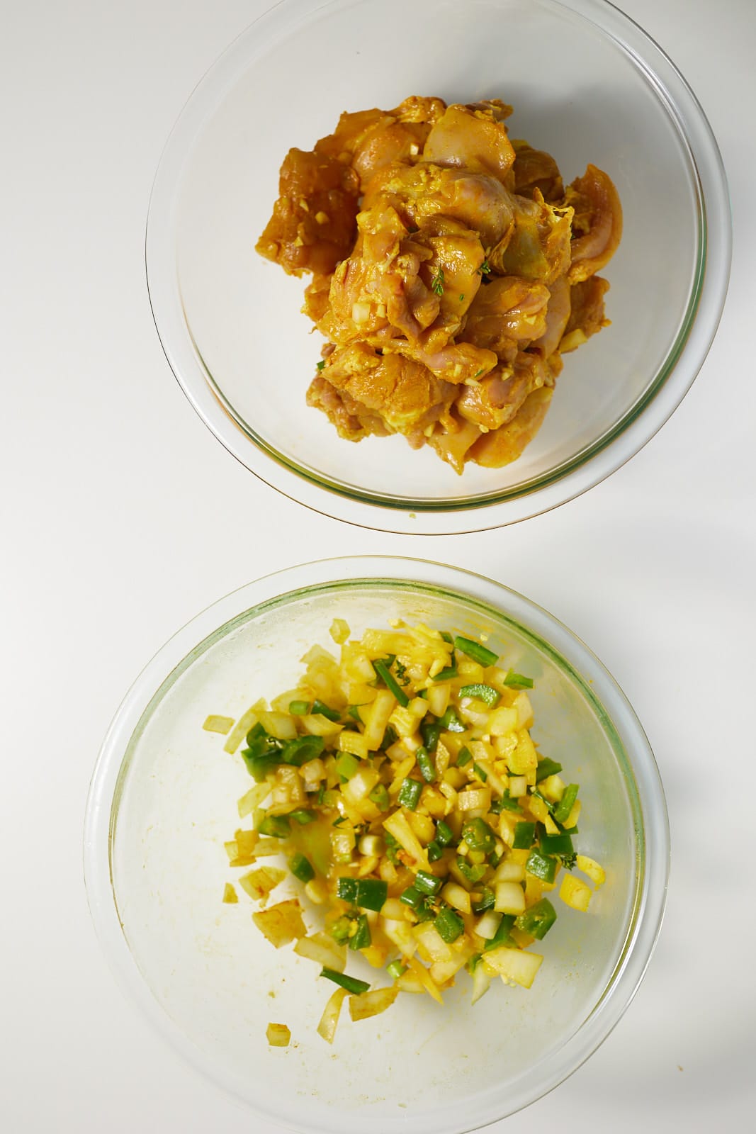 Marinated chicken in one bowl and onions, peppers and garlic in another.