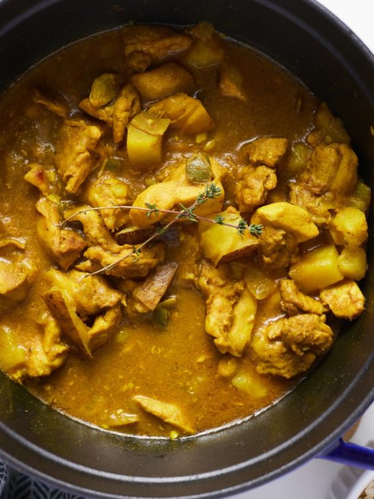 Jamaican curry chicken in blue pot with spoon on side
