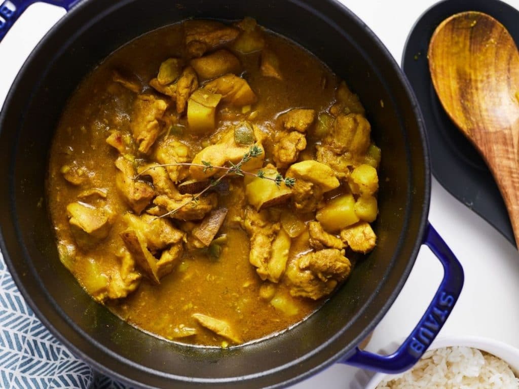 jamaican curry chicken in blue pot with a wooden spoon on the side