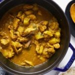 jamaican curry chicken in blue pot with a wooden spoon on the side