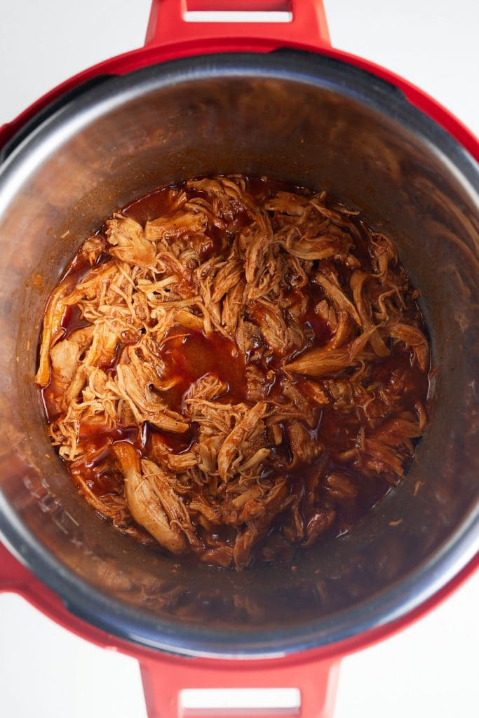 BBQ sauce being stirred into the shredded chicken.