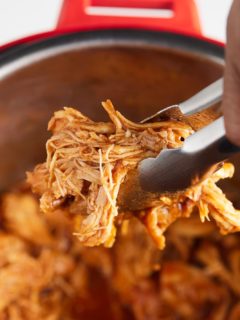 Shredded BBQ chicken being picked up with tongs.