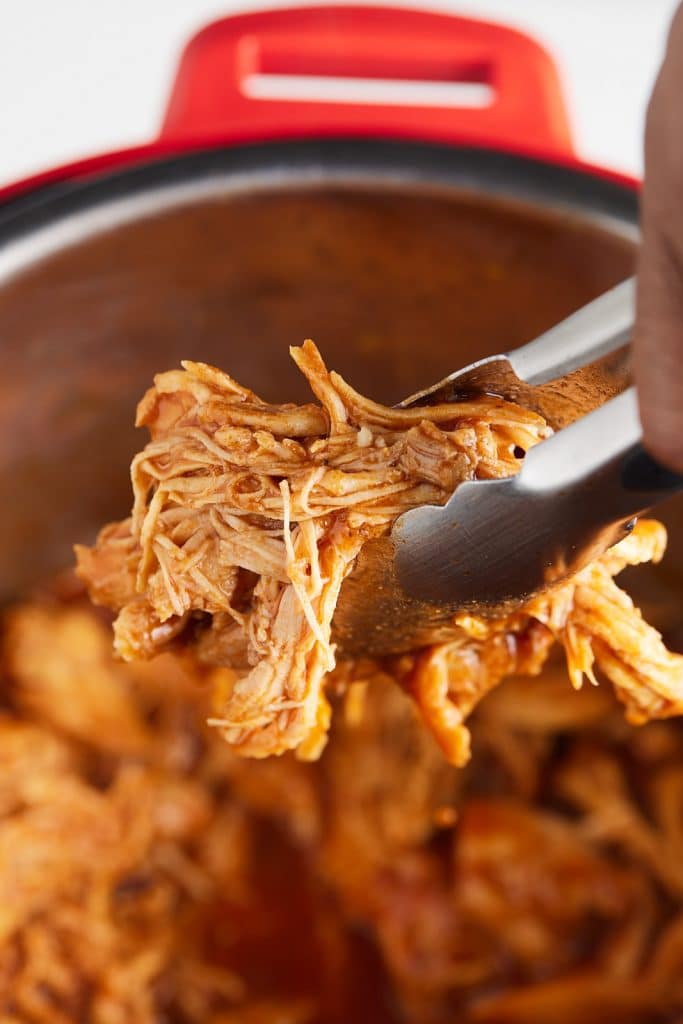 Shredded BBQ chicken being picked up with tongs.