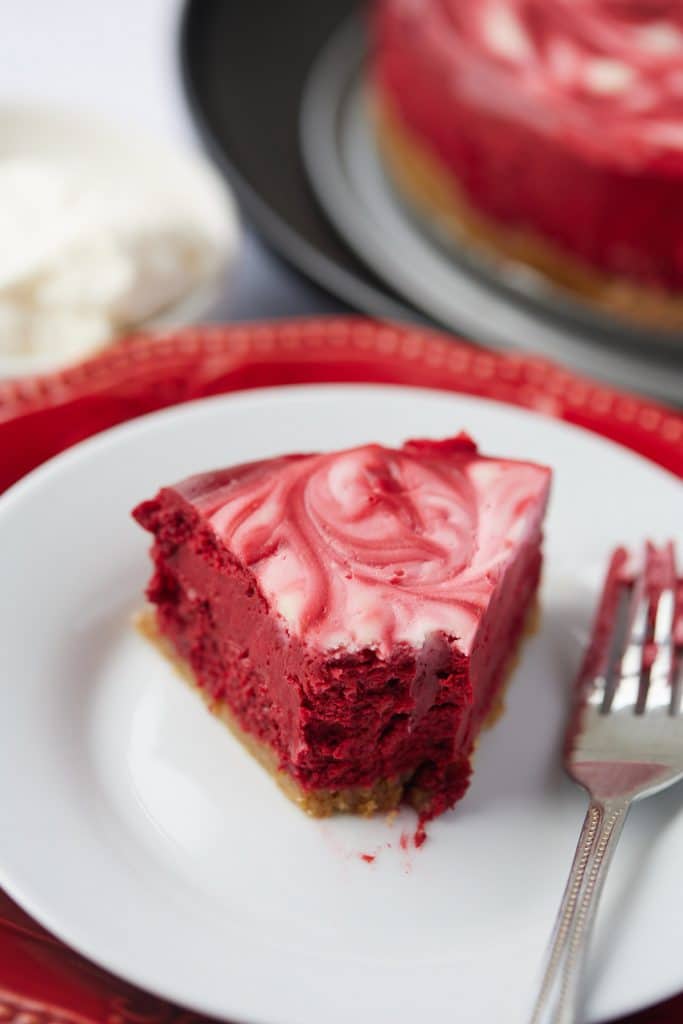 A slice of red velvet cheesecake with the end cut off with a fork.