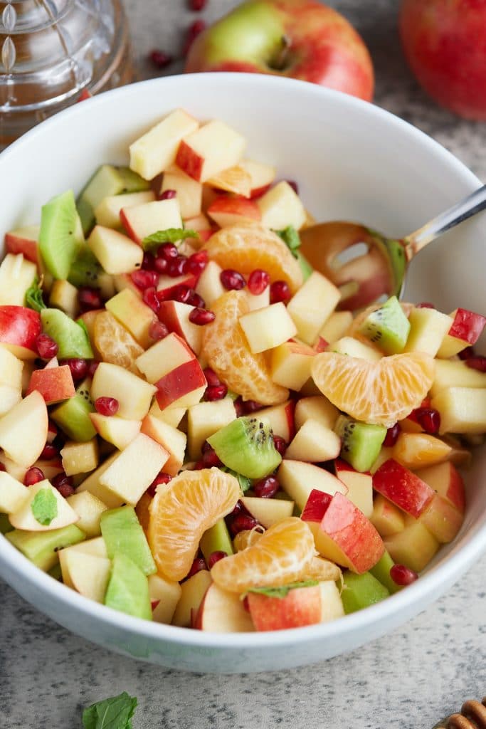 white bowl with fruit salad inside of it with spoon sticking out in corner