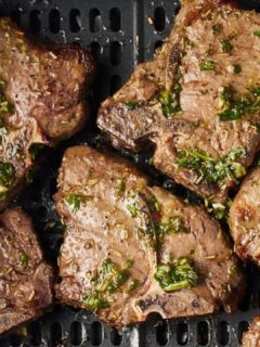 air fryer lamb chops in the air fryer basket covered with chimichurri sauce