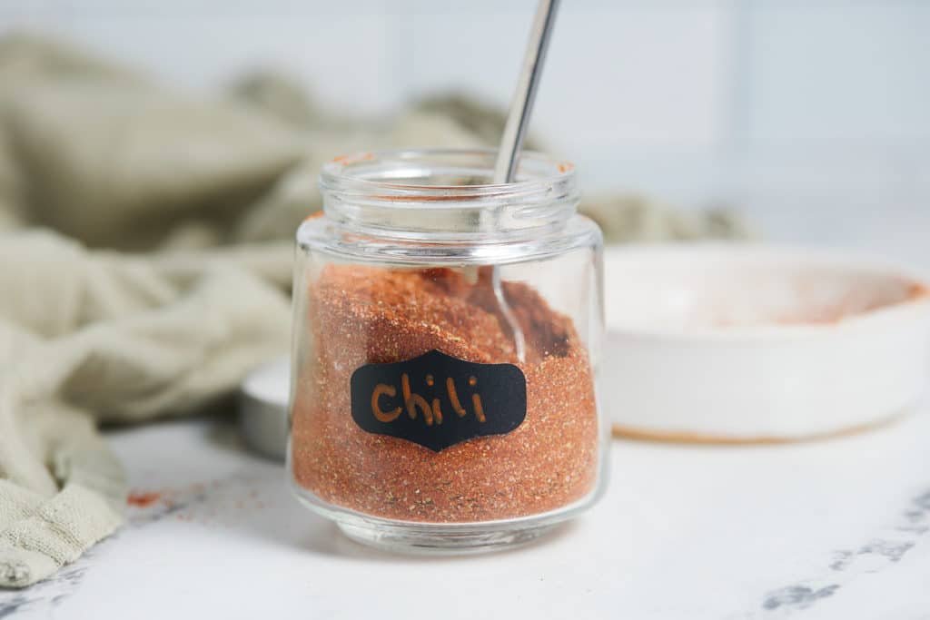 Chili powder in a glass jar with a spoon.
