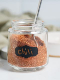 Chili powder in a glass jar with a spoon.