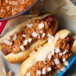 Hot dogs topped with chili on a blue plate.