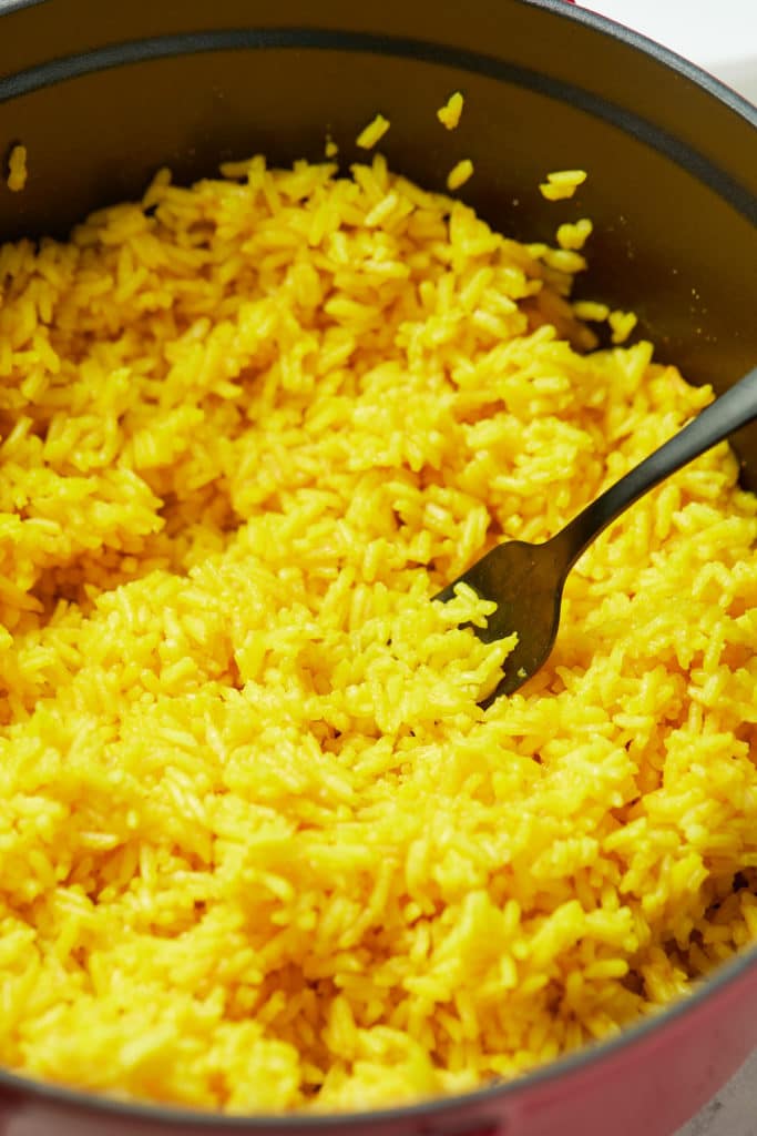 A fork fluffing the turmeric rice.