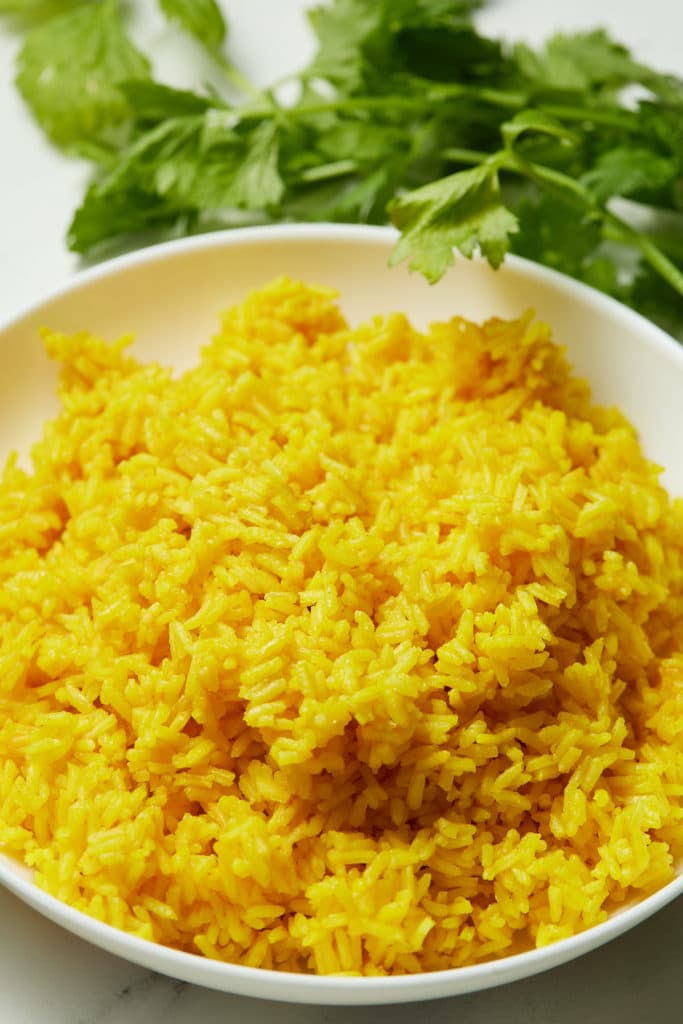 Yellow rice served on a white plate next to fresh herbs.