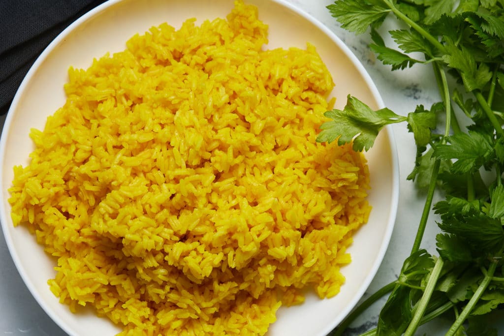 Yellow rice on a white plate next to fresh cilantro.