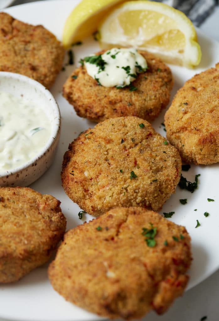Six salmon patties on a plate served with sour cream and a wedge of lemon.