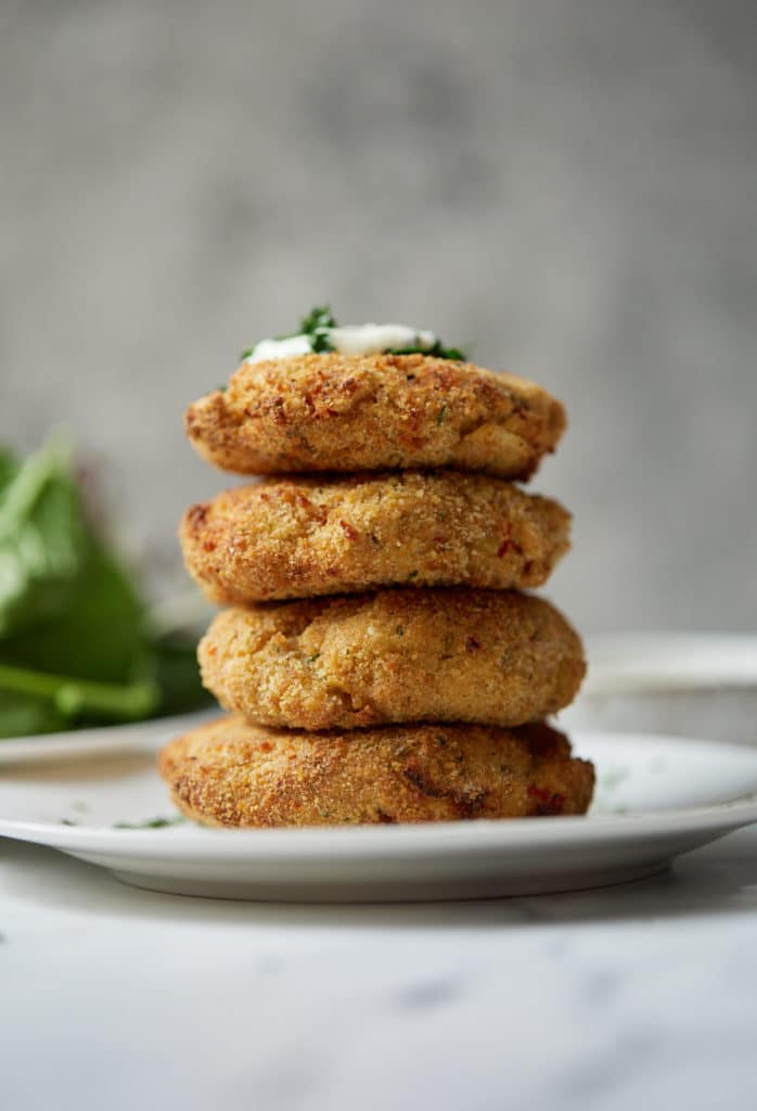 Four salmon patties stacked on top of each other and topped with tartar sauce