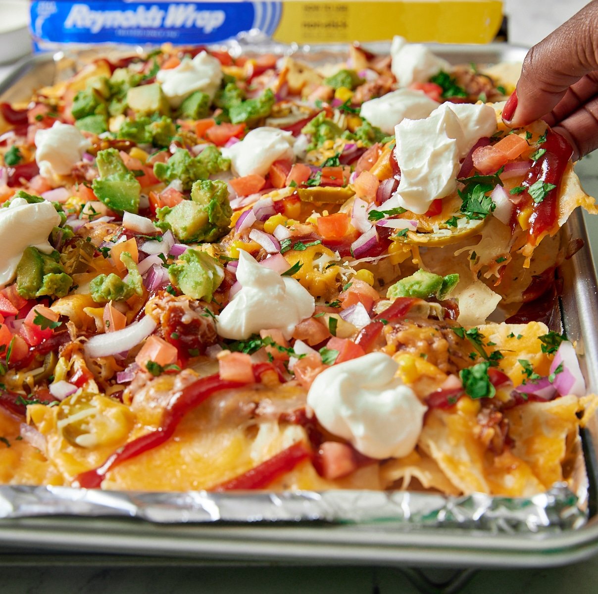 hand pulling up nacho chip with Reynolds® Wrap Non-Stick foil box in background