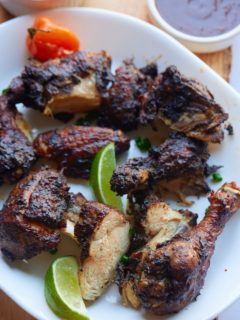 Jerk chicken served on a plate with lime wedges.