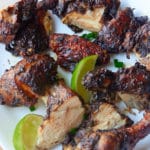 Chopped Jamaican jerk chicken served on a plate with lime wedges.