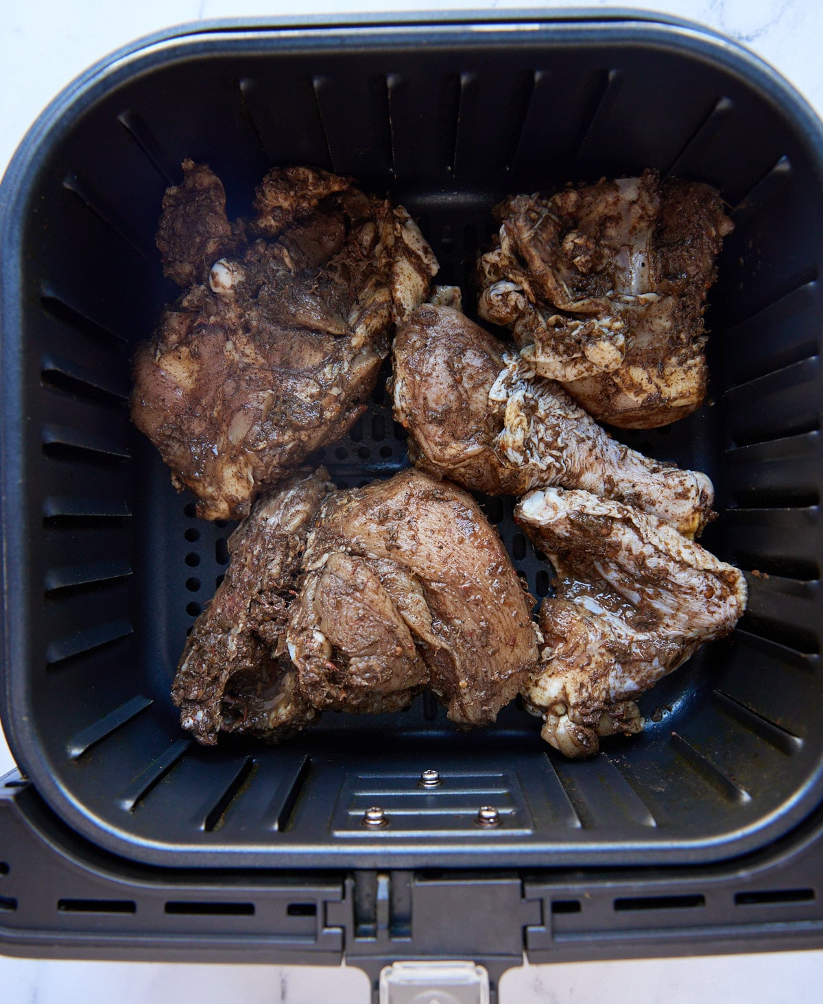 The marinated chicken in an air fryer basket.