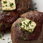 Two sous vide filet mignon steaks on a white plate topped with butter.